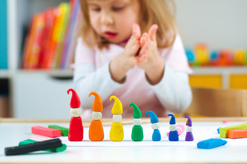 Girl molding colorful gnomes from childs play clay on the table