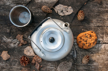 Aluminum teapot , cup, cones, dry leaves and oatmeal cookies with chocolate on dry wooden table. Flat lay food. Picnic. Outdoor cooking. Kettle. Spring background. Autumn background. Picnic concept 