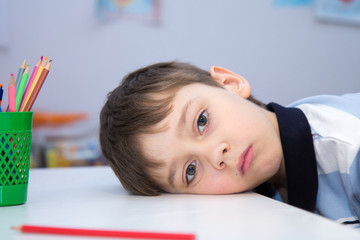 The boy's head is lying on a white Desk, the child is sad. It is boring to be alone during...
