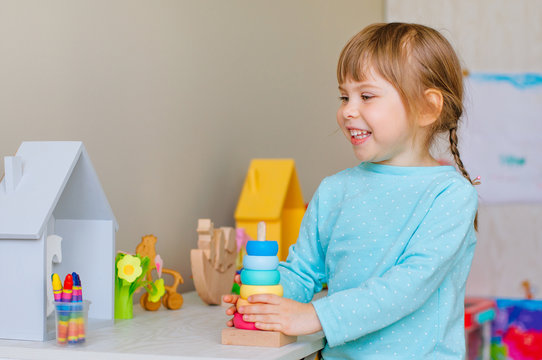 Happy little toddler girl playing with colorful wooden pyramid toy