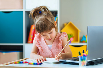 Beautiful little girl writing homework using notebook for distance learning