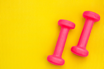Pink dumbbells on the background of a yellow yoga mat. The concept of a sports lifestyle, weight loss, exercise, energy, charging emotions. Top view. Copy space.