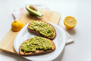 toasted bread with avocado paste. Avocado mixed with lemon juice is spread on bread. toast with avocado lies on a white plate and wooden cutting board. health food concept, vegan, vegetarian
