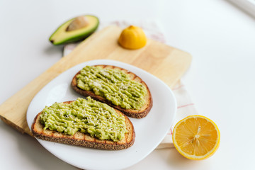 toasted bread with avocado paste. Avocado mixed with lemon juice is spread on bread. toast with avocado lies on a white plate and wooden cutting board. health food concept, vegan, vegetarian