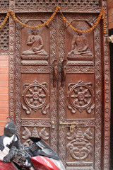 Old carved brown wooden door with sitting Buddha in Thamel district of Kathmandu city. Theme of decorations on the doors.