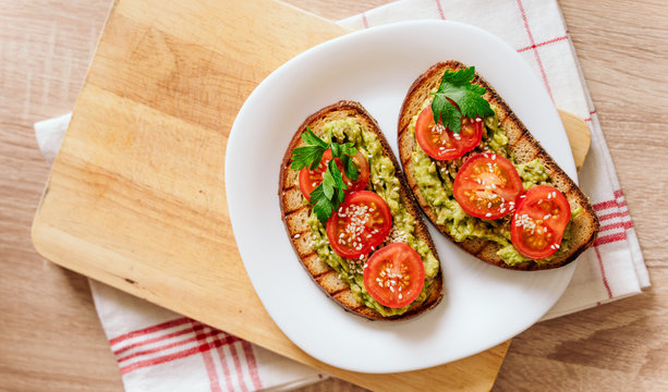 toasted bread with avocado paste and fresh tomato. Avocado mixed with lemon juice is spread on bread. health food concept, vegan, vegetarian - Powered by Adobe