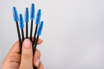 Set of eyelash brushes in hand on white background. Copy space for text. Blue, black eyelash brush in hand girl master eyelash extension. Professional beauty makeup tools for eyelashes and eyebrows.