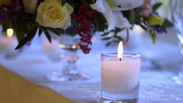Beautiful close up of romantic candle on a dinner table with colorful flowers at the background