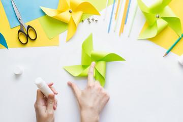 How to make paper green windmill toy with children at home. Step by step instructions. Hands making DIY summer project. Top view. Step 8. Glue remaining corners, overlaying each other.