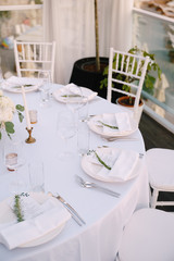 Wedding dinner table reception. Close-up of a round wedding table with white plates and a menu enclosed in a napkin. The devices lie next to the plate according to the requirements of etiquette.