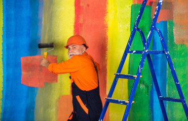 senior man painter use roller on ladder. painting the wall colorful. professional painter in...