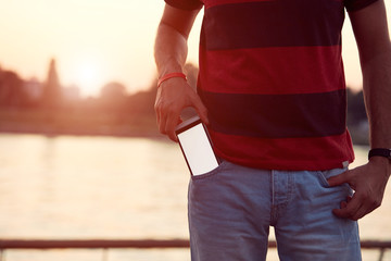 Man holding cellphone in pocket near river.