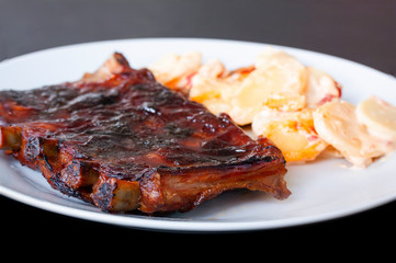 Spicy hot grilled spare ribs from BBQ served on a plate with paprika scalloped potatoes. Close-up image