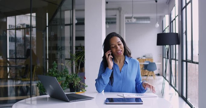 Successful African American female employee calling by mobile phone for discussing work project in digital format on touch pad. Dark skinned business woman while work in office interior. 4K RED camera