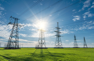 High voltage lines and power pylons and a green agricultural landscape on a sunny day.