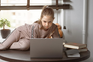 Cool online school. A child learns online at home using a laptop. Cheerful little girl using laptop...