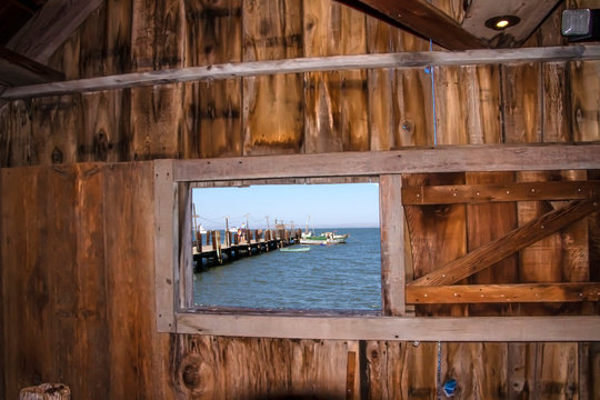 Blue ocean view with a pier and a boat from seen through a window inside an old wood shack  Royalty free stock photo