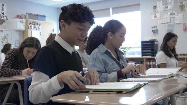 High school students talking and studying at desks in classroom