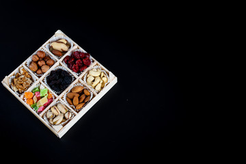 Assorted dried fruits and nuts in a wooden box isolated on a black background. Raisins, candied fruits, cherries, Brazil nuts, hazelnuts, walnuts, almonds, cashews, pistachios.