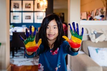 Asian girl with hands painted with rainbow paint at home