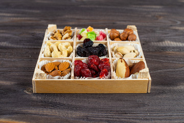 Assorted dried fruits and nuts in a wooden box isolated on a dark wood background. Raisins, candied fruits, cherries, Brazil nuts, hazelnuts, walnuts, almonds, cashews, pistachios.