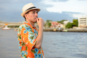 Young handsome tourist man thinking at pier against view of the river