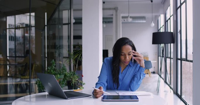 African American female entrepreneur calling by smartphone for consulting about project while using stylus pencil and tablet. Business woman working in office interior. Slow motion on 4k RED camera
