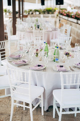 Fototapeta na wymiar Wedding dinner table reception. Round banquet table with white tablecloth and white Chiavari chairs. Wedding under the tent. 