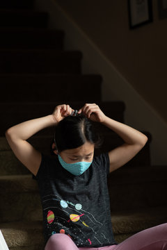 Asian girl looks down while tying on face mask