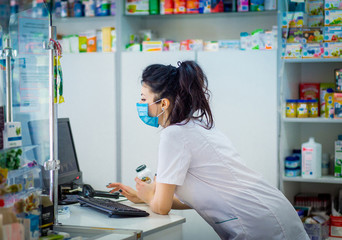 the pharmacist is holding a container with medicine and is studying it. A pharmacist in a medical mask on his face punches medicine in a computer.