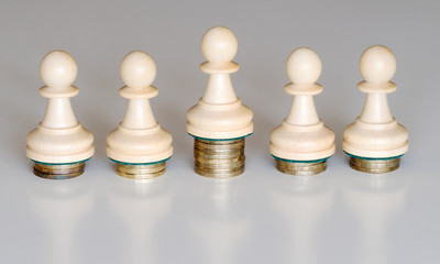 Five pawns of chess pieces on columns of coins symbolizing the exclusion from equal income