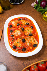 Pan seared fish with tomatoes and olives on an brown table. Selected focus.