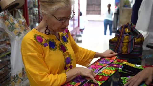 Closeup of mature woman wearing ethnic clothing looks at colorful cinturon belts in a shop in Merida, Mexico.