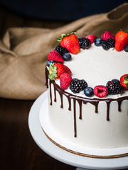 Beautiful white cake .Decorate with fruits-strawberries, raspberries, blackberries,blueberries, chocolate.Handmade work.White porcelain high stand