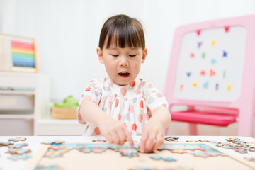 Fototapeta premium toddler girl playing wooden puzzle at home