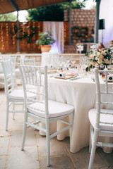 Fototapeta na wymiar Wedding dinner table reception. A close-up of the white classical chair for Chiawari's wedding, Tiffany near the round table, amid the lights of the garland