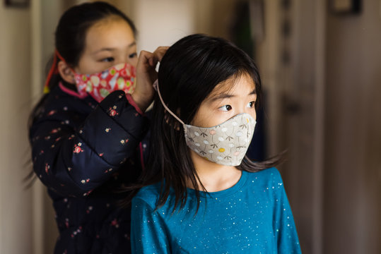 Girl tying strings of mask for her sister