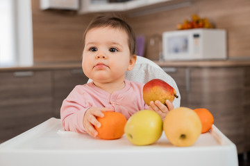 Toddler girl sits in a child's chair in the kitchen eating vegetables