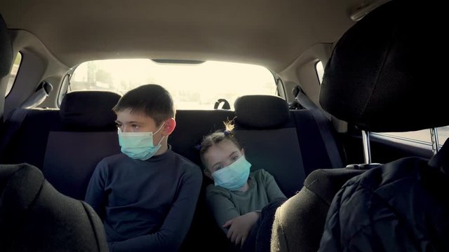 Boy and girl in protective face masks on back seat of moving car in city traffic. Brother nad sister fith father during coronavirus epidemic and self isolation. Stop COVID-19 infection and pandemic