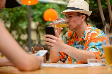 Happy multi ethnic tourist couple using phone at restaurant