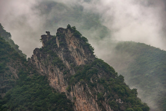 Baidicheng, China - May 7, 2010: Qutang Gorge on Yangtze River. Landscape of gray cloudscape descends in waves along slopes of green covered mountains, one beigh sharp topped.