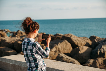 Fototapeta na wymiar young woman photographs the sea and rocks on her mobile phone
