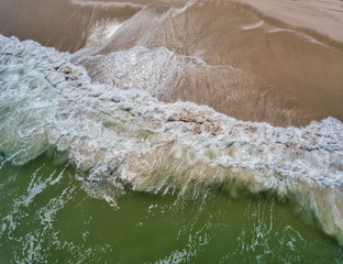 Aerial drone image of foamy waves washing up on the beautiful sandy beach of Island Beach State Park in New Jersey creating colorful abstract images