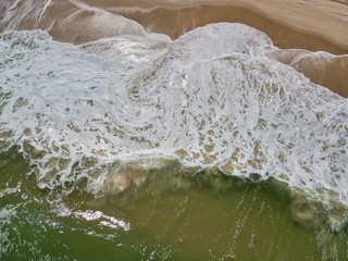 Aerial drone image of foamy waves washing up on the beautiful sandy beach of Island Beach State Park in New Jersey creating colorful abstract images
