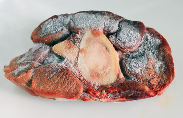 A piece of frozen meat with a bone, steak on white background. Shortages of beef, pork and chicken meat due to the pandemic of coronavirus COVID-19 in some countries. 