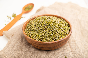 Wooden bowl with raw green mung bean and wooden spoon on a white  background. Side view, selective focus.