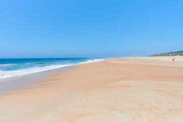 Fototapeta na wymiar Long sandy beach on a sunny day at Nazaré norte beach