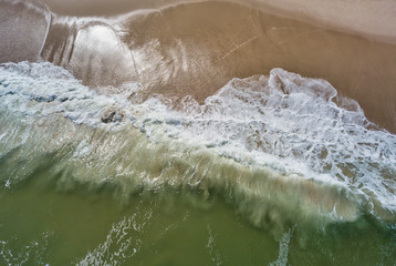 Obraz na płótnie Canvas Aerial drone image of foamy waves washing up on the beautiful sandy beach of Island Beach State Park in New Jersey creating colorful abstract images