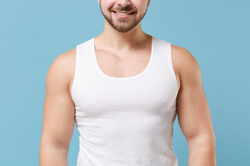 Cropped image of strong smiling young bearded guy 20s in white singlet posing isolated on pastel blue wall background studio portrait. Sport fitness healthy lifestyle concept. Mock up copy space.