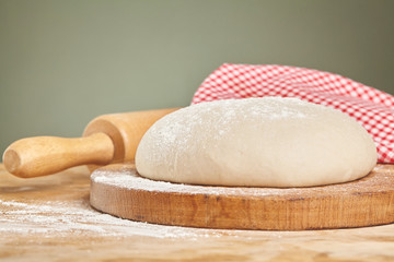 Wooden rolling pin on dough over cutting board at table. Close up.
